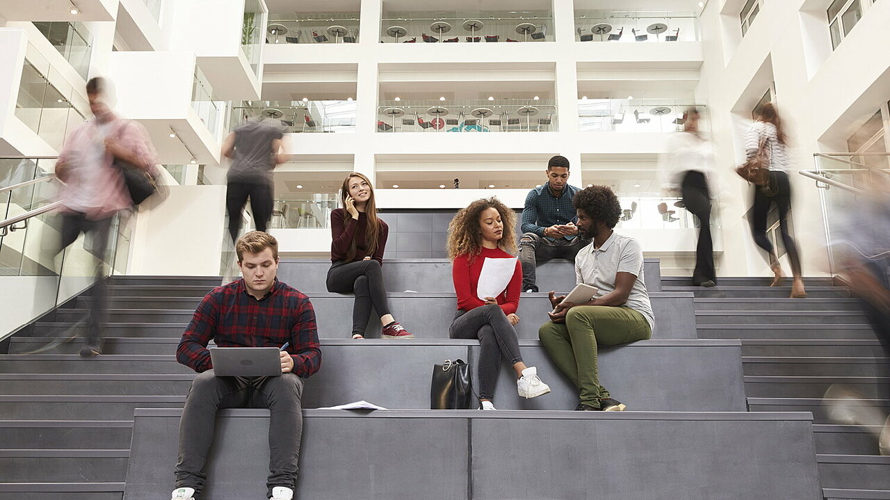 Junge Studierende sitzen auf den Treppenstufen eine Hochschule