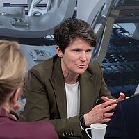 Drei Personen unterhalten sich. Zwei sieht man nur von hinten.