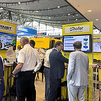 Mehrere Personen auf einem Messestand, die sich unterhalten und Exponate anschauen