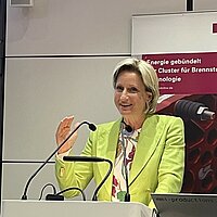 Dr. Nicole Hoffmeister-Kraut, Ministerin für Wirtschaft, Arbeit und Tourismus in Baden-Württemberg, steht vor einem Rednerpult und hebt die Hand.