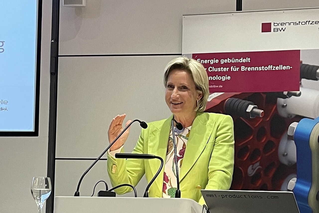 Dr. Nicole Hoffmeister-Kraut, Ministerin für Wirtschaft, Arbeit und Tourismus in Baden-Württemberg, steht vor einem Rednerpult und hebt die Hand.