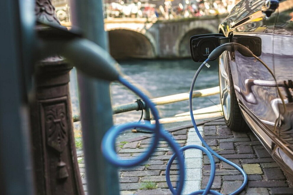 Ein E-Auto beim Laden an einer Ladesäule in der Stadt am Ufer eines Gewässers.