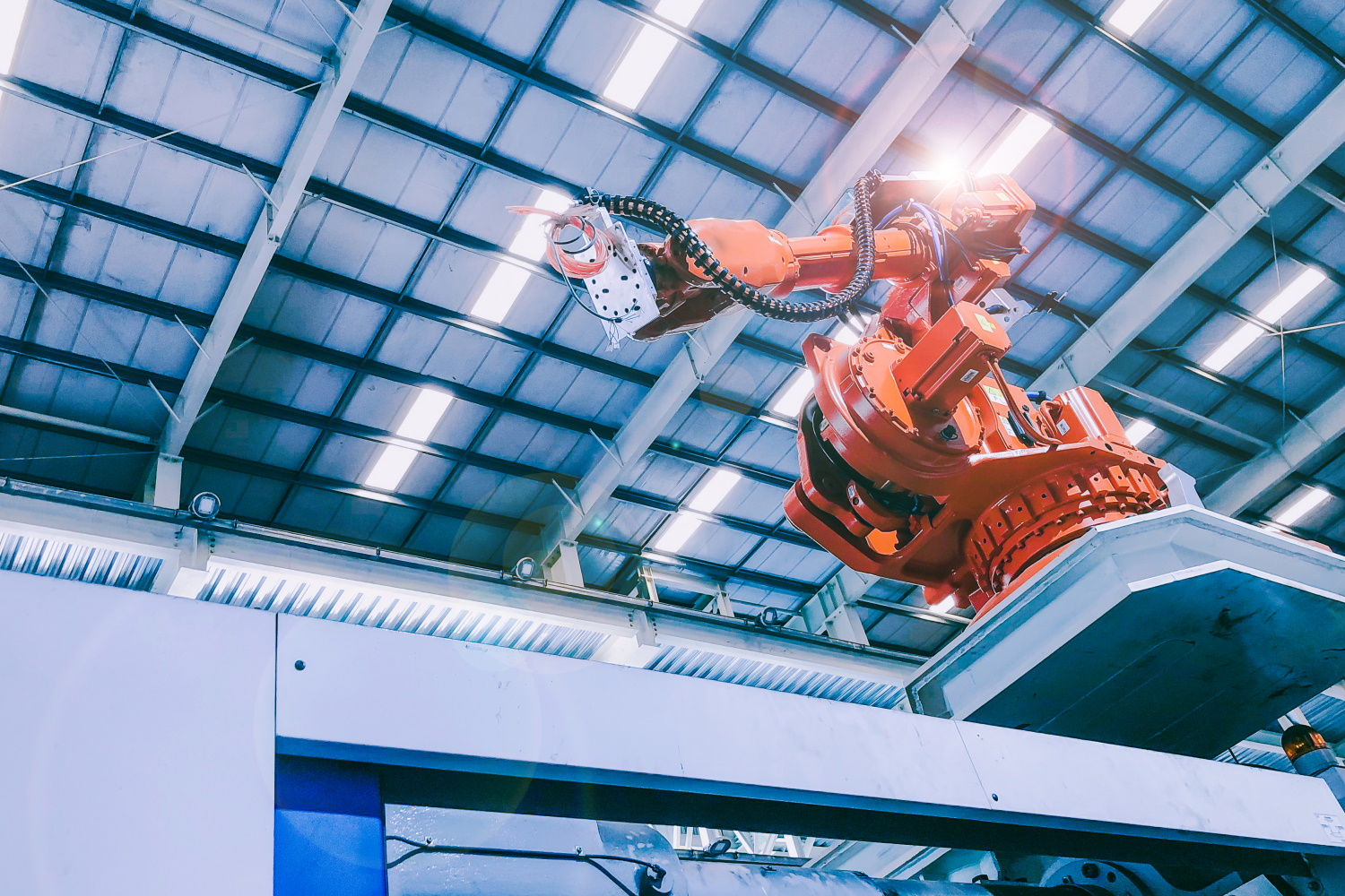 Arm eines orangefarbenen Industrie-Roboters in einer Produktionshalle.