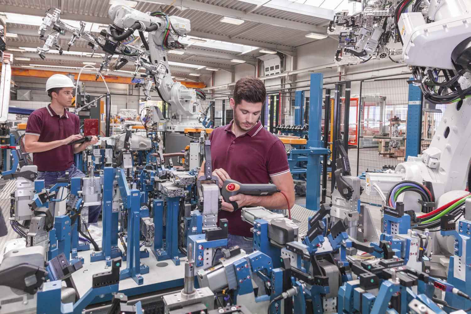 Zwei Arbeiter in einer Produktionsstätte bedienen jeweils einen weißen Roboterarm
