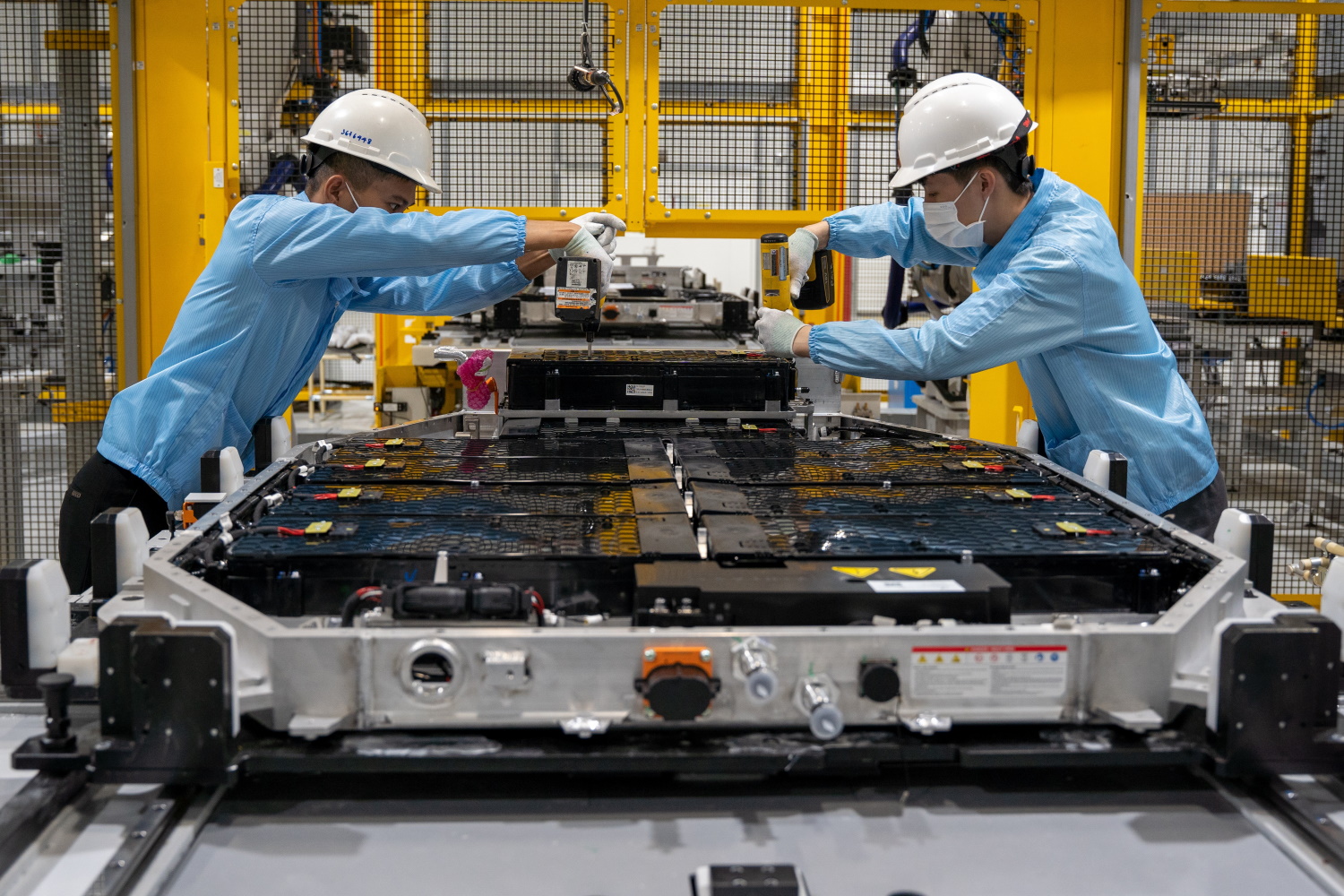 Zwei Menschen arbeiten in einer Fabrik an einer Batterie für Elektrofahrzeuge. 