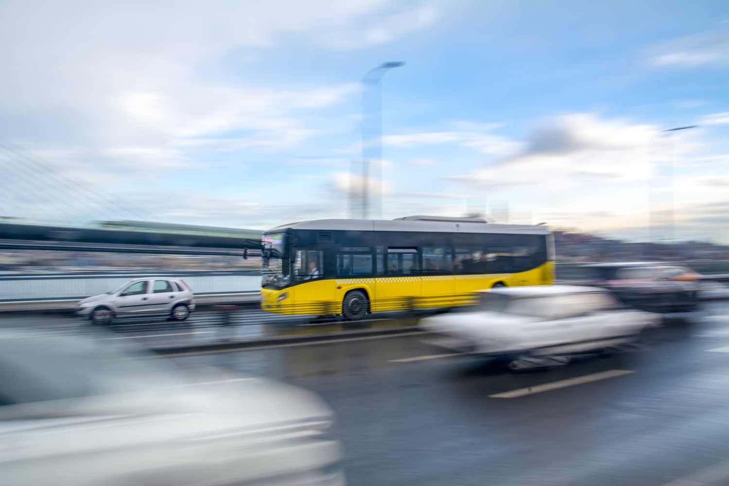 Ein gelber Bus fährt schnell auf einer mehrspurigen Straße. Auf den anderen Spuren sieht man verschwommen Autos.