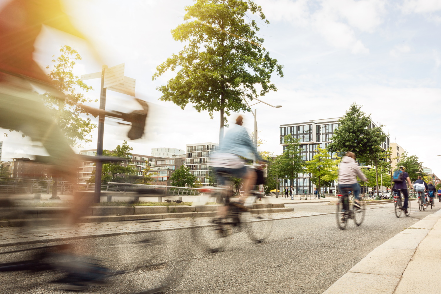 Eine Gruppe von Fahrradfahrern fährt auf einem Radweg an modernen Gebäuden vorbei. 