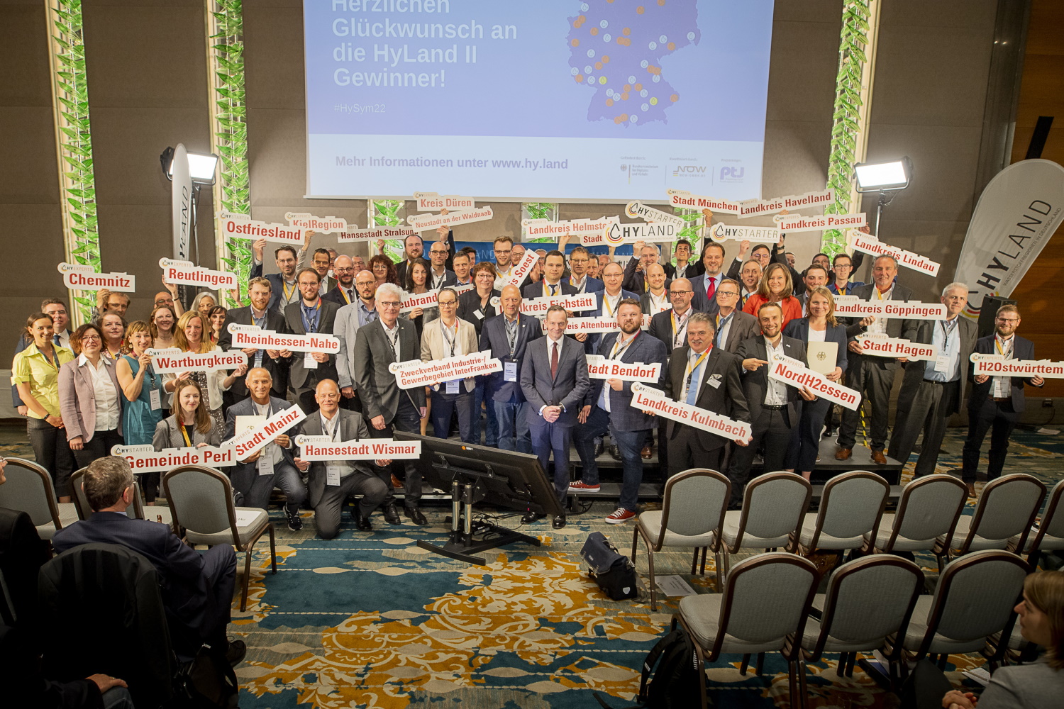 Gruppenfoto der ausgezeichneten Regionen mit Verkehrsminister Wolfgang Wissing. Die Namen der Regionen sind auf Schildern lesbar, die durch Regionalvertrerinnen und -vertreter hochgehalten werden.