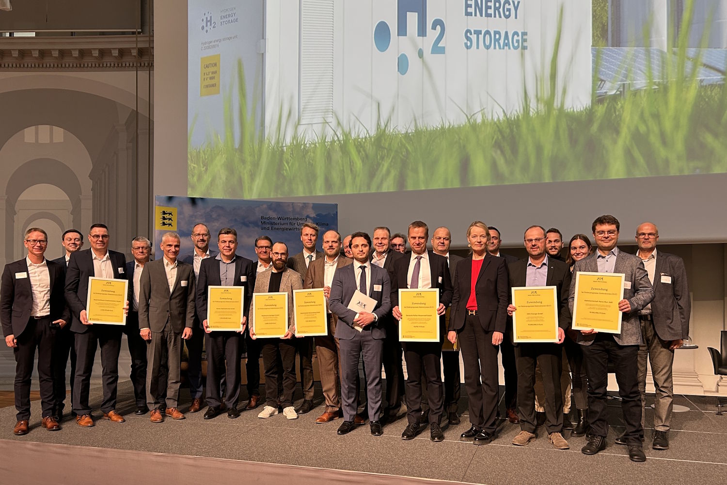 Repräsentanten der ELY-Projekte stehen mit den Verträgen in der Hand gemeinsam auf der Bühne bei der Förderübergabe in Stuttgart. 