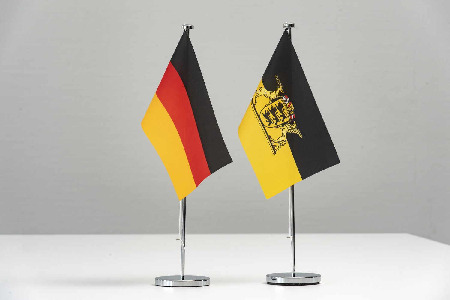 Flaggen von Deutschland und Baden-Württemberg stehen als Wimpel auf einem weißen Tisch.