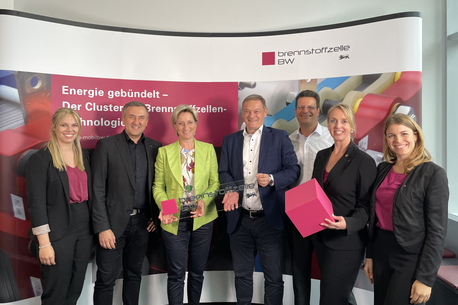 Das Team des Clusters Brennstoffzelle BW posiert gemeinsam mit Baden-Württembergs Wirtschaftsministerin Dr. Nicole Hoffmeister-Kraut vor einem großen Cluster BZ Aufsteller 