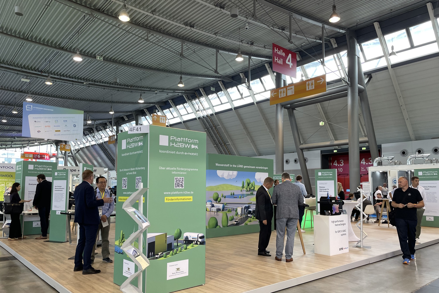 Messestand der Plattform H2BW. Grüne Informationssäulen und einzelne Exponate an denen sich die Messebesuchenden unterhalten.