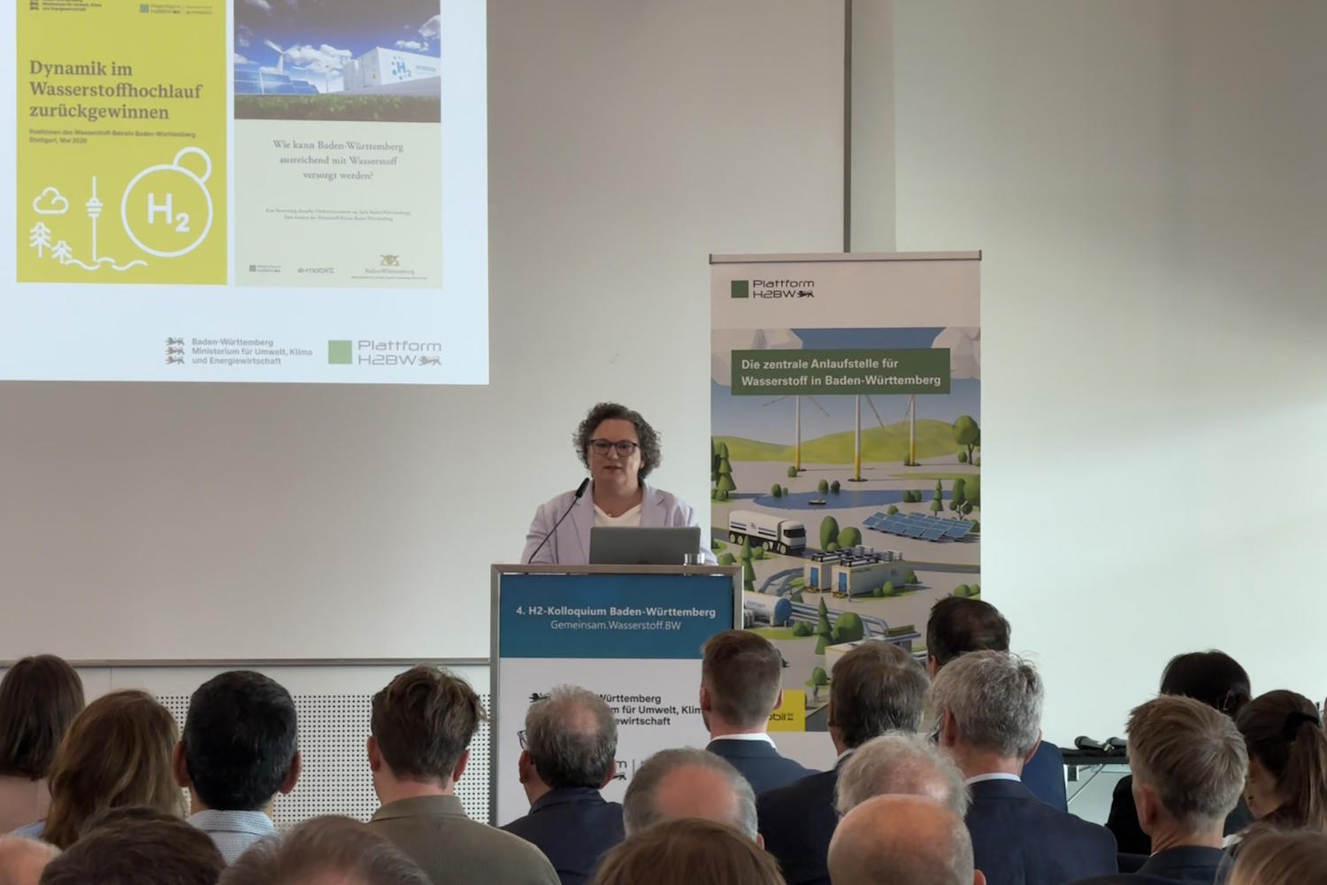 Eine Frau referiert, das Publikum sitzt vor ihr. 
